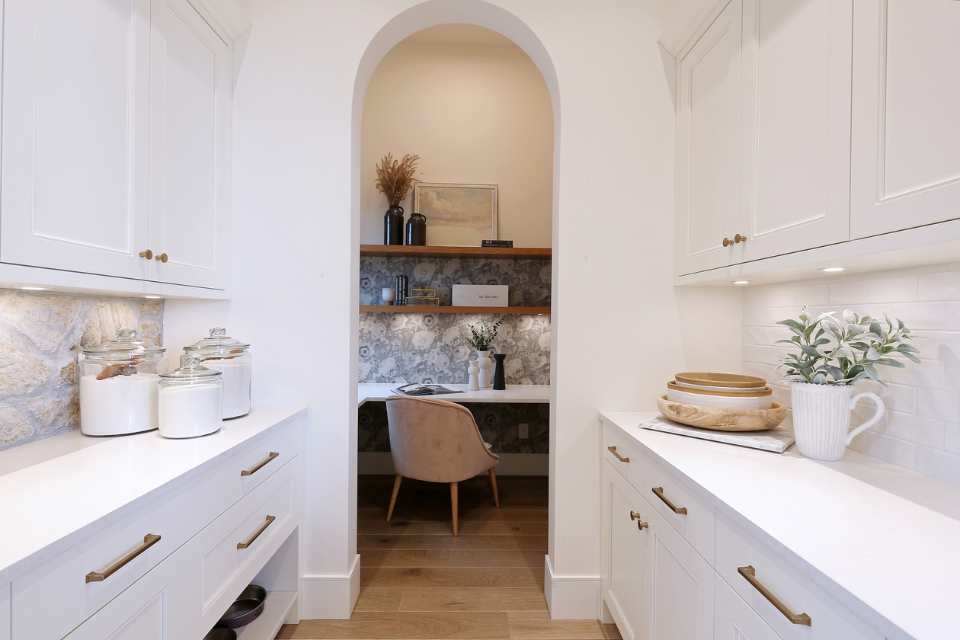 hidden office nook with wallpaper and shelving through butler's pantry of designer white kitchen